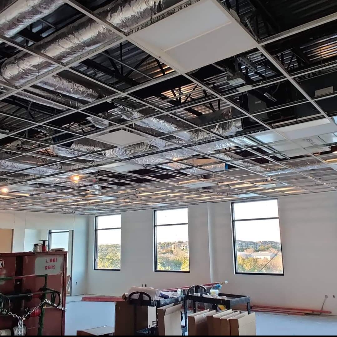 Under-construction office interior with exposed ceiling grid, ductwork, and partially installed ceiling tiles.