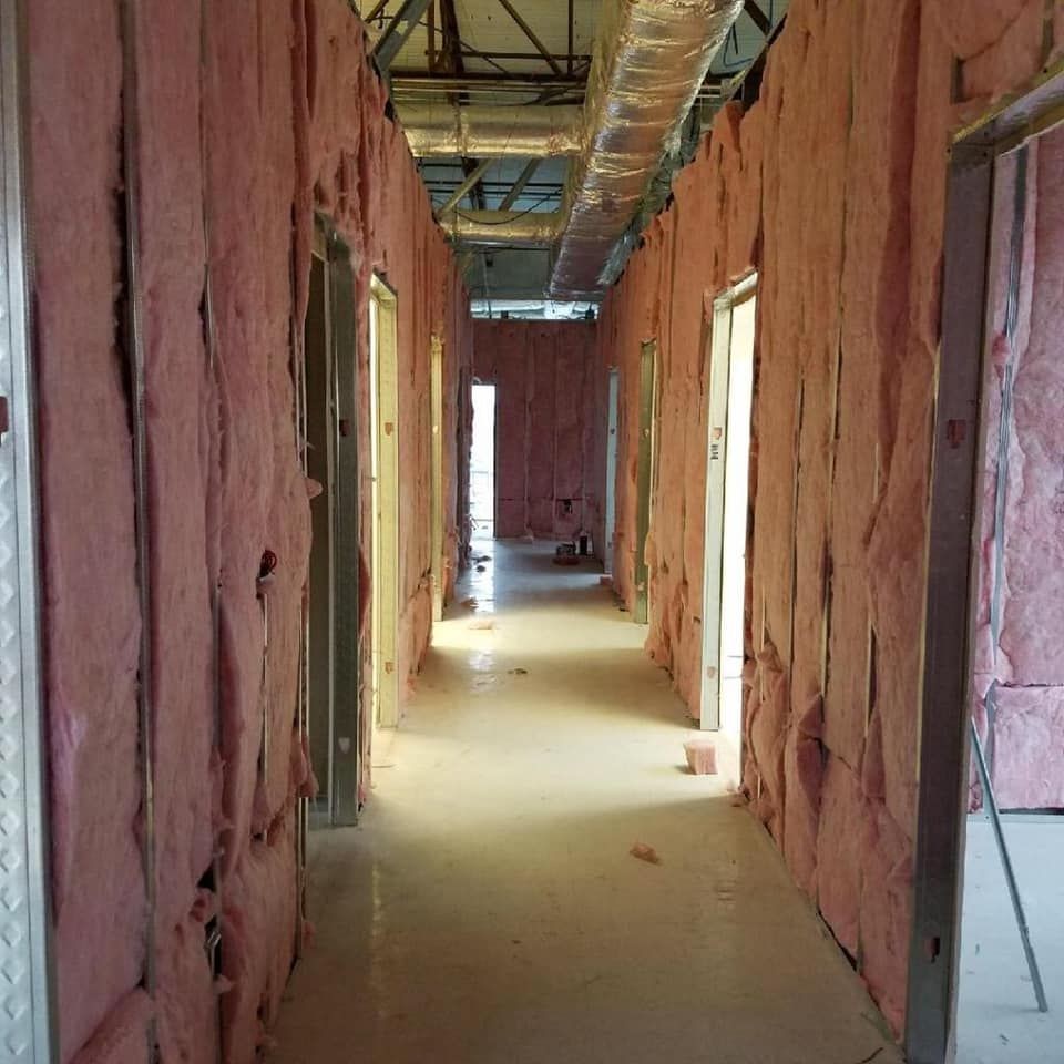 Corridor under construction with exposed pink insulation on the walls and visible ceiling ducts.